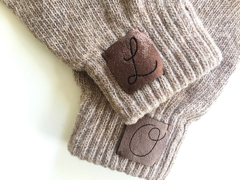 Puede incluir: Dos gorros de punto marr&oacute;n con parches de cuero marr&oacute;n. Los parches tienen las letras "L" y "O" bordadas en hilo negro.