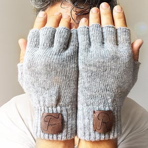 May include: A pair of gray fingerless gloves with brown leather patches on the cuffs. The patches have the letters "F" and "R" engraved on them.