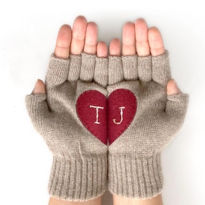 May include: A pair of beige fingerless gloves with a red heart on the back. The heart has the initials "TJ" embroidered on it.