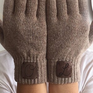 Puede incluir: Un par de guantes de punto marr&oacute;n con parches de cuero en los pu&ntilde;os. El guante izquierdo tiene una letra "O" en el parche y el guante derecho tiene una letra "L" en el parche.