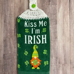 May include: Green kitchen towel with a white crocheted hanging loop and a green button. The towel features a gnome with a green hat and a shamrock in its hand. The text "Kiss Me I'm IRISH" is printed on the towel.
