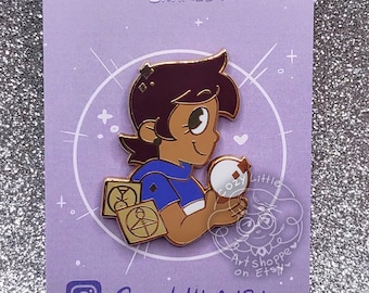 May include: A purple and white enamel pin featuring a cartoon character holding a glowing orb. The character has brown hair, a blue shirt, and a gold symbol on their chest. The pin says "Glyph Magic Enamel Pin" at the top and "CozyLittleArtBlog" and "CozyLittleArtShoppe" at the bottom.