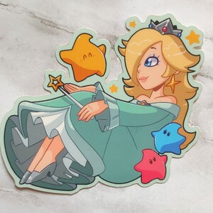 May include: A sticker featuring a cartoon character with blonde hair, a crown, and a blue dress. The character is holding a wand and surrounded by stars. The sticker is on a light gray marble background.