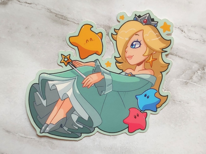 May include: A sticker featuring a cartoon character with blonde hair, a crown, and a blue dress. The character is holding a wand and surrounded by stars. The sticker is on a light gray marble background.