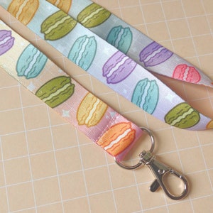 May include: A colourful lanyard with a repeating pattern of macarons. The lanyard has a silver metal clip.