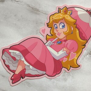 May include: A pink and white cartoon character with blonde hair and a crown, wearing a pink dress and holding a pink and white mushroom umbrella. The character is surrounded by pink hearts.