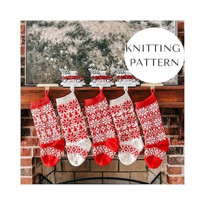May include: Five red and white knitted Christmas stockings with snowflake patterns hang from a fireplace mantel. Above the stockings are decorative red trucks carrying Christmas trees. The image includes the text "KNITTING PATTERN".