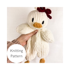 Peut inclure: Jouet en peluche blanc tricoté en forme de canard avec un nœud rouge et un bec orange. Le jouet est tenu par une main. Le texte "Knitting Pattern" est écrit dans un cercle sur l'image.