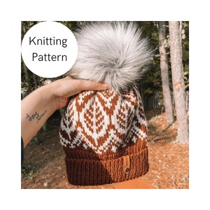 Peut inclure: Un bonnet en tricot marron et blanc avec un motif géométrique et un pompon en fausse fourrure blanche. Le bonnet a une étiquette en cuir marron avec le mot "Stitched" dessus.