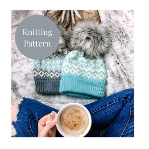 May include: Two knitted hats with a geometric pattern, one blue and one grey, with faux fur pom poms. The hats are on a fluffy white surface with a cup of coffee in the foreground.
