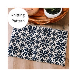 May include: Knitting pattern for a black and white patterned scarf. The scarf is laid out on a wooden surface.