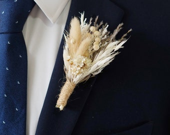 May include: A dried flower boutonniere with a natural, rustic look. The bouquet features dried grasses and white flowers, tied with twine.