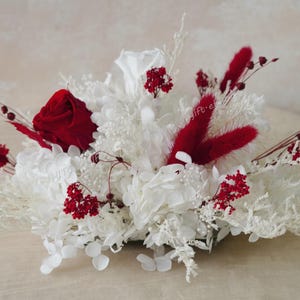 Puede incluir: Un ramo de flores secas con una rosa roja y flores blancas. El ramo está adornado con hierbas secas rojas.