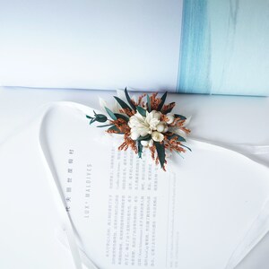 May include: A white and brown dried flower arrangement with green leaves, tied with a white ribbon. The arrangement is on a white book with the text "LUX MALDIVES" printed on the cover.
