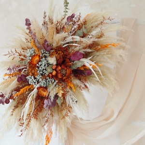 Könnte beinhalten: Eine getrocknete Blumenarrangement mit Pampasgras, getrockneten Blumen und Eukalyptus in den Farben Beige, Braun, Orange und Lila.