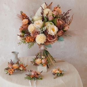 Può includere: Un bouquet da sposa e accessori abbinati con fiori color pesca, crema e marrone. Il bouquet è grande e legato con un nastro. Gli accessori includono un pettine per capelli, corsetti e un'occhiello.