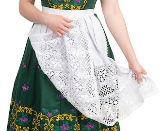 Pode incluir: Uma mulher vestindo um vestido tradicional bávaro verde com detalhes em renda branca e bordados florais. Ela está segurando o avental em suas mãos e olhando para baixo.