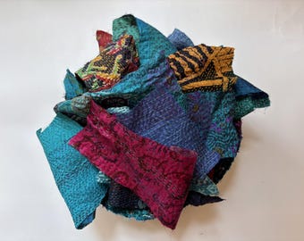 May include: A collection of assorted fabric scraps featuring kantha stitching. The pieces display a variety of colors including magenta, teal, blue, and yellow, with intricate patterns and textures visible across the layered, overlapping textile fragments.