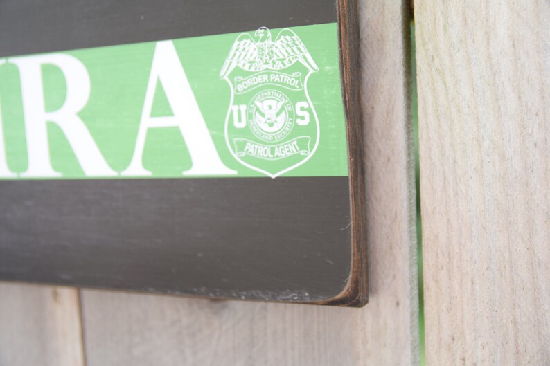May include: A wooden sign with a green stripe and the words "U.S. BORDER PATROL PATROL AGENT" in white. The sign is on a wooden background.