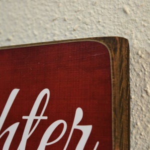 Puede incluir: Primer plano de un letrero de madera rojo con letras blancas que dice "la risa es la mejor medicina". El letrero tiene un marco de madera desgastado.