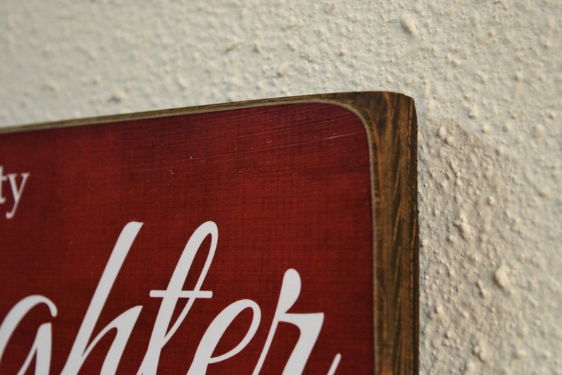 Puede incluir: Primer plano de un letrero de madera rojo con letras blancas que dice "la risa es la mejor medicina". El letrero tiene un marco de madera desgastado.