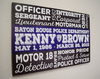 May include: A black and blue wooden sign with white text honoring a police officer. The sign reads "Officer, Integrity, Sergeant, Corporal, Lieutenant, Motorman, Hero, Courage, Baton Rouge Police Department, Kenny Brown, May 1, 1986 - March 26, 2015, Honor, Pride, Motor 18, Brave, Protect & Serve, Detective, Police Officer."