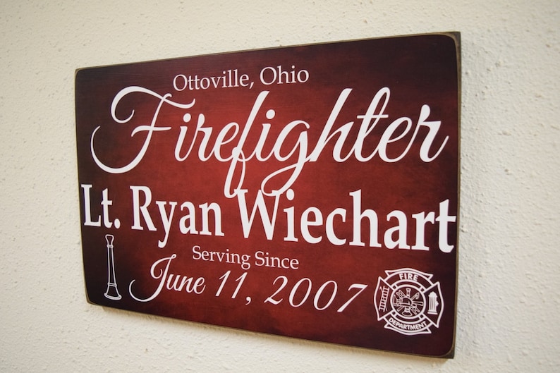 Puede incluir: Un letrero de madera rojo con texto blanco que dice "Ottoville, Ohio Firefighter Lt. Ryan Wiechart Serving Since June 11, 2007". Un logotipo blanco del departamento de bomberos est&aacute; en la esquina inferior derecha.