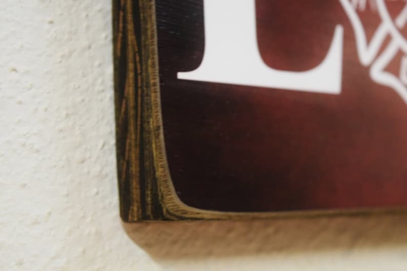 Puede incluir: Primer plano del borde de un letrero de madera con un marco de madera marr&oacute;n oscuro. El letrero tiene un fondo rojo con letras blancas.