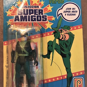 May include: Green Arrow action figure from the Super Amigos collection. The figure is packaged in a plastic blister pack with a yellow and blue background. The packaging features the text "Flecha Verde" and "¡CON MI SUPER ARCO Y FLECHA!" The figure is wearing a green and black costume with a green hood and a quiver of arrows on his back.