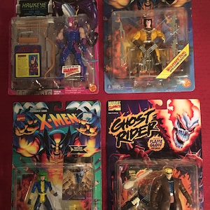 May include: Four action figures in their original packaging. The figures are from the Marvel Comics universe and include Hawkeye, Wolverine, Polaris, and Blaze. The packaging features bright colors and bold graphics.