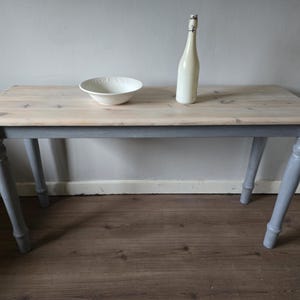 May include: A rectangular wooden table with a light-coloured top and grey legs. A white ceramic bowl and a white bottle with a swing top are on the table. The table is approximately 122 cm long.
