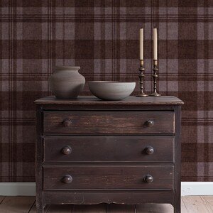 May include: A dark brown wooden dresser with three drawers, topped with a ceramic vase, a bowl, and two brass candle holders with lit candles. The background features a brown and gray plaid pattern.