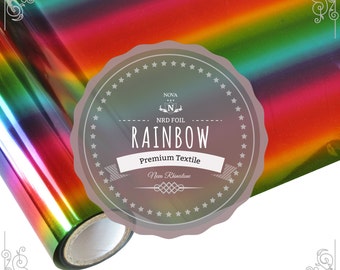May include: A roll of rainbow holographic heat transfer vinyl for crafting projects. The vinyl is iridescent and has a metallic sheen. The label reads "Nova NRD Foil Rainbow Premium Textile Non-Rhinestone".