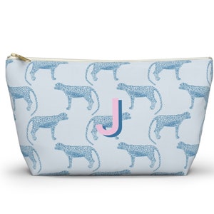 May include: A light blue zippered pouch with a repeating pattern of blue leopard print. The pouch has a pink and blue letter "J" in the center.