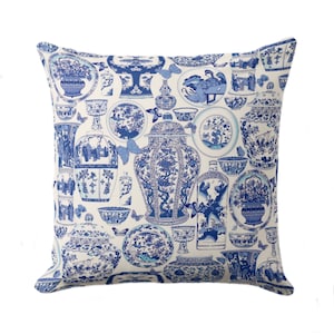 May include: A white cushion with a blue and white pattern of Chinese porcelain vases, bowls, and plates. The pattern is repeated throughout the cushion.