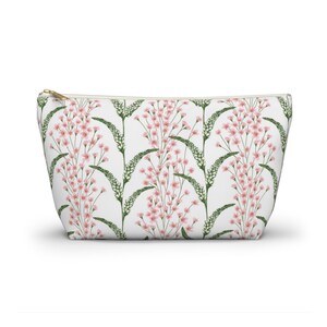 May include: A white zippered pouch with a floral pattern. The pattern features pink flowers and green leaves on a white background.