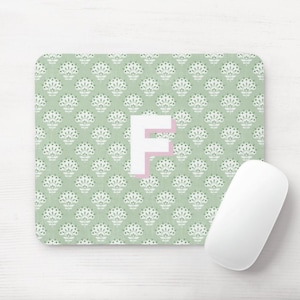 May include: A green mousepad with a white floral pattern and the letter "F" in the center. The letter is outlined in pink.