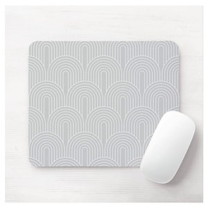 May include: A gray mouse pad with a white geometric pattern of overlapping arches. The mouse pad is on a white wooden surface.