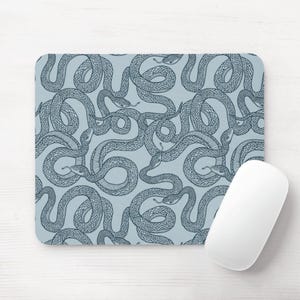 May include: A rectangular mouse mat featuring a repeating pattern of detailed, dark blue snakes on a light blue background. A white computer mouse is positioned on the right. The snakes are intertwined, creating a unique design.