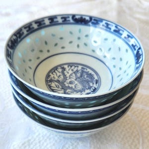 May include: A stack of four white porcelain bowls with blue decorative patterns. The bowls have a blue dragon design in the center and a blue border. The bowls are stacked on top of each other.