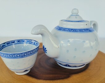 May include: A white teapot and teacup set with blue and white floral designs. The teapot has a round body and a spout with a curved handle. The teacup is round and has a small handle.