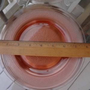 May include: A pink glass dessert plate with a raised floral design. The plate measures 8 inches in diameter.