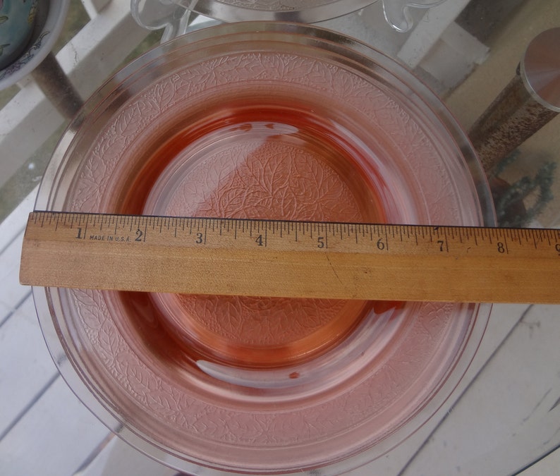 May include: A pink glass dessert plate with a raised floral design. The plate measures 8 inches in diameter.