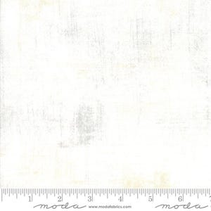 May include: White fabric with a subtle, distressed texture. The fabric has a slightly off-white color with a hint of gray. The fabric is shown with a ruler, indicating it is for quilting or sewing projects.