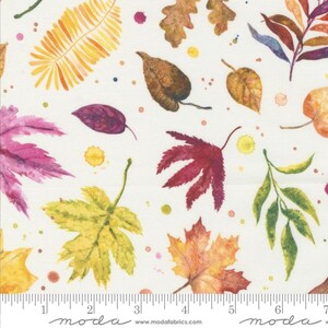 May include: A white fabric with a repeating pattern of colorful leaves and splattered paint. The leaves are in shades of red, orange, yellow, green, and purple. The fabric is marked with a ruler in inches and the words "moda" and "modafabrics.com".