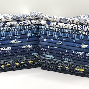 May include: Two stacks of folded fabric squares in various shades of blue and cream. The patterns include floral motifs, stripes, bird illustrations, geometric shapes, and celestial designs with small yellow accents on the bottom layers.