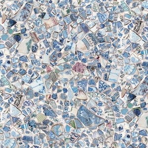 May include: A close-up of a mosaic made of broken pieces of blue and white china. The mosaic is set in white grout and has a variety of patterns and designs.