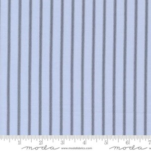 May include: Pale blue fabric featuring vertical grey stripes. The stripes are evenly spaced and run the length of the material. The fabric has a subtle texture and a ruler is at the bottom of the image.