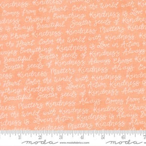 May include: Peach-colored fabric with white cursive text repeating phrases like "Kindness Matters" and "Scatter seeds of Kindness." The fabric has a subtle texture and a ruler along the bottom edge.