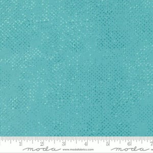 May include: Teal fabric with a white speckled pattern. The fabric is measured with a ruler in inches. The text "moda" is printed on the ruler.